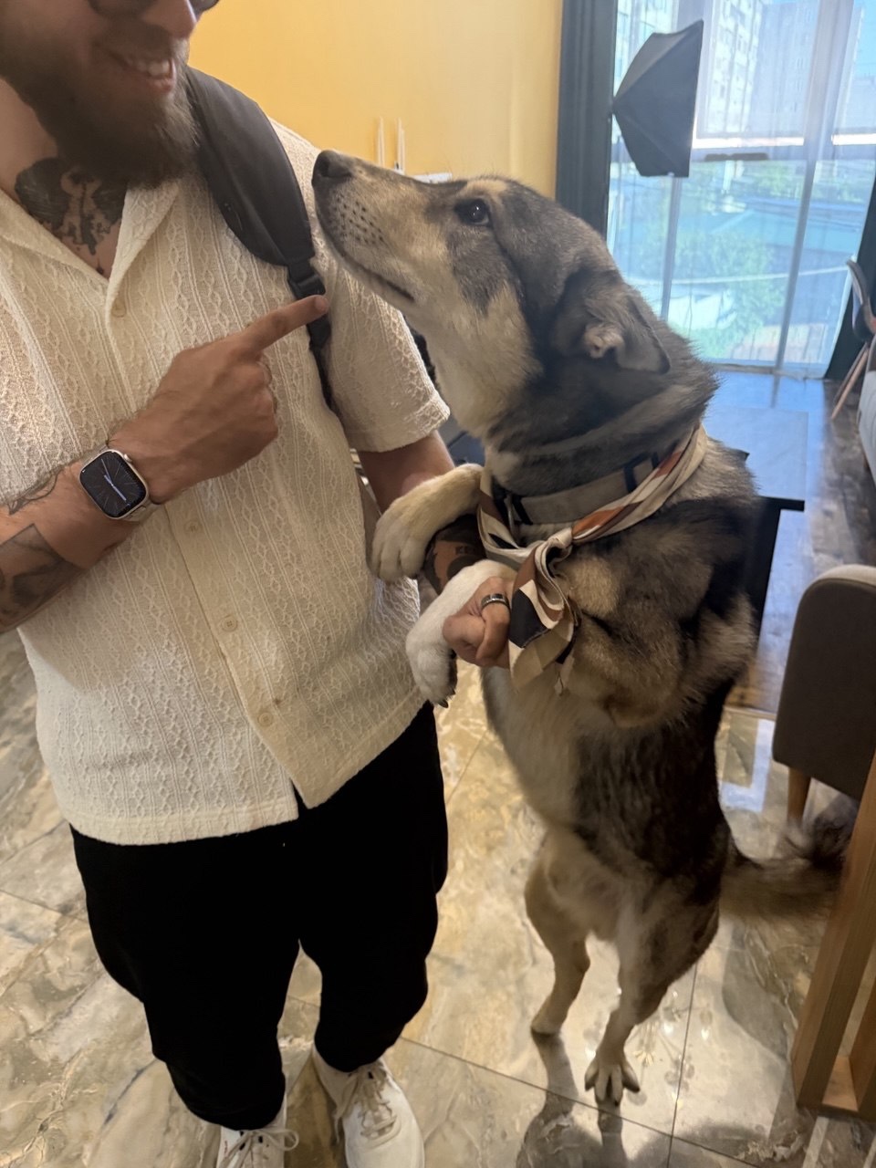 Denis in a white shirt, holding the paw of a dog standing beside him.